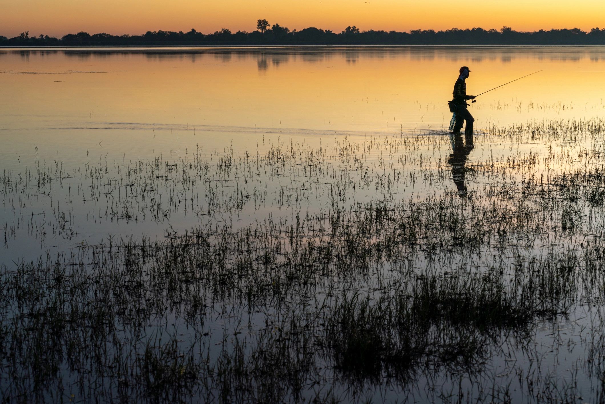 Silhouette of an angler fishing on a lake at sunrise