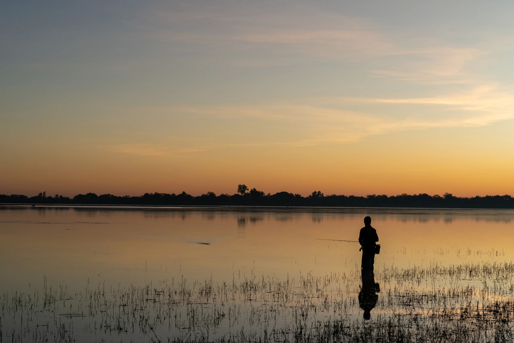 Silhouette of a fisherman at dawn on a lake