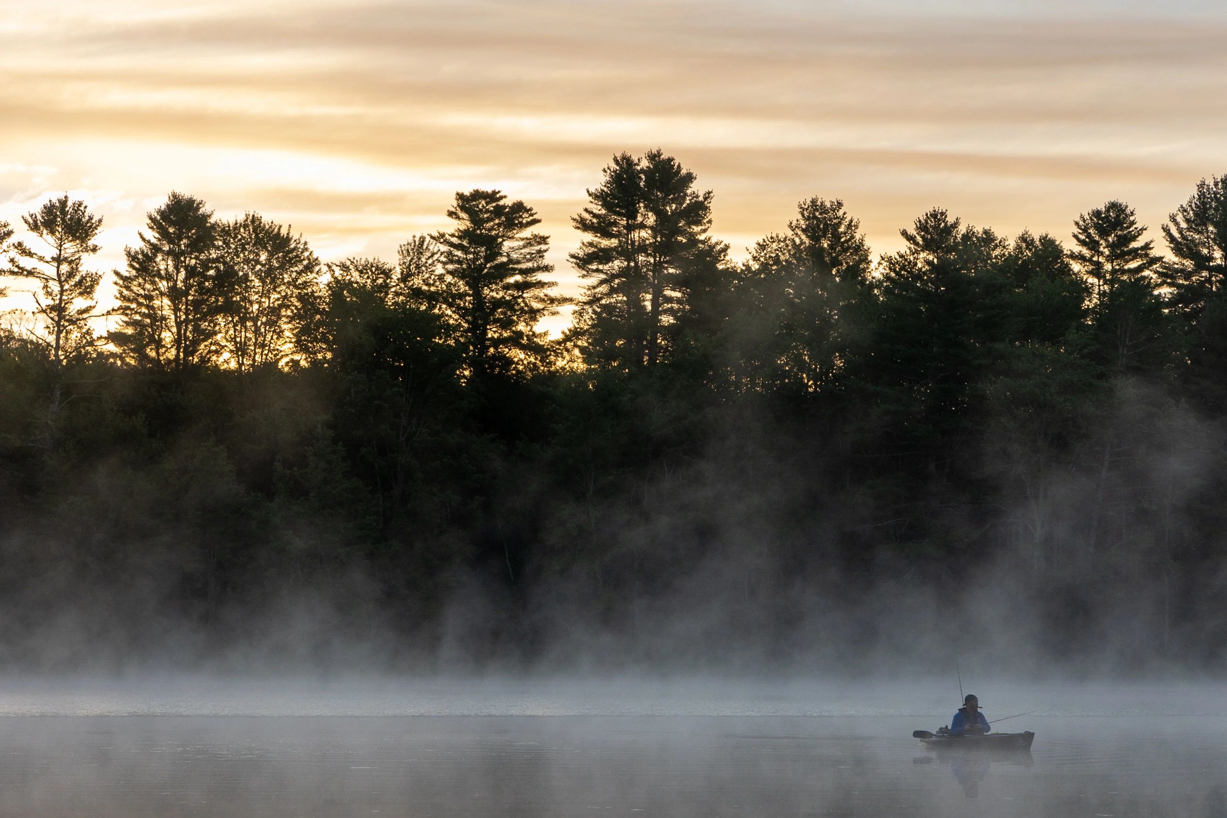 Kayak anglers fishing on a foggy lake at sunrise