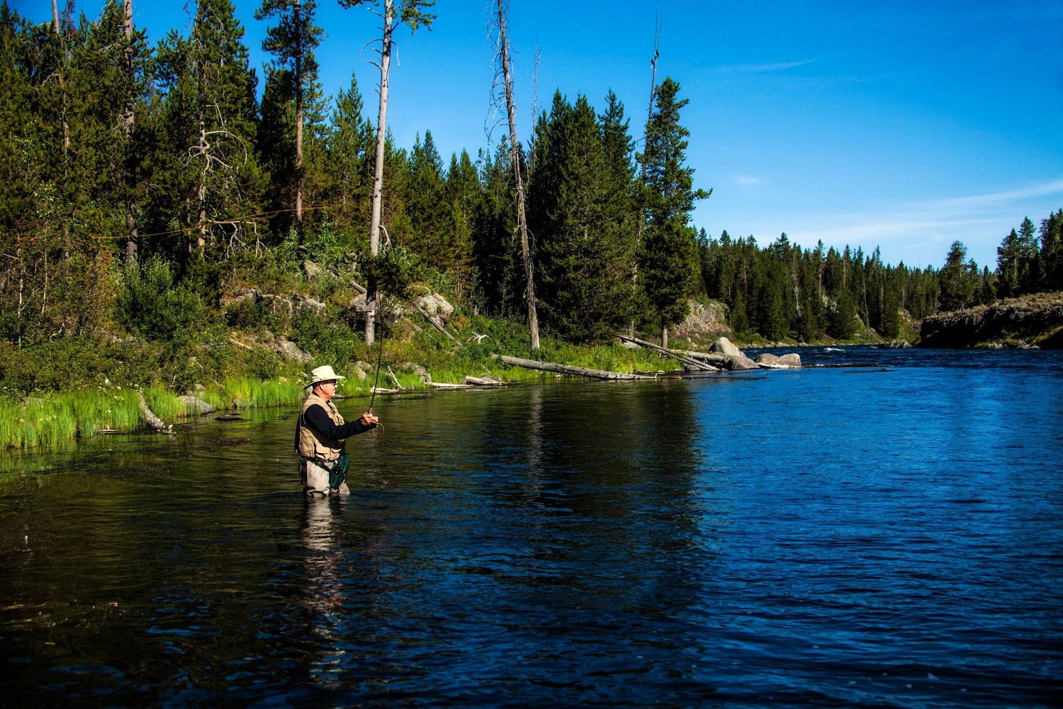Fly fisherman casting a line into a clear river