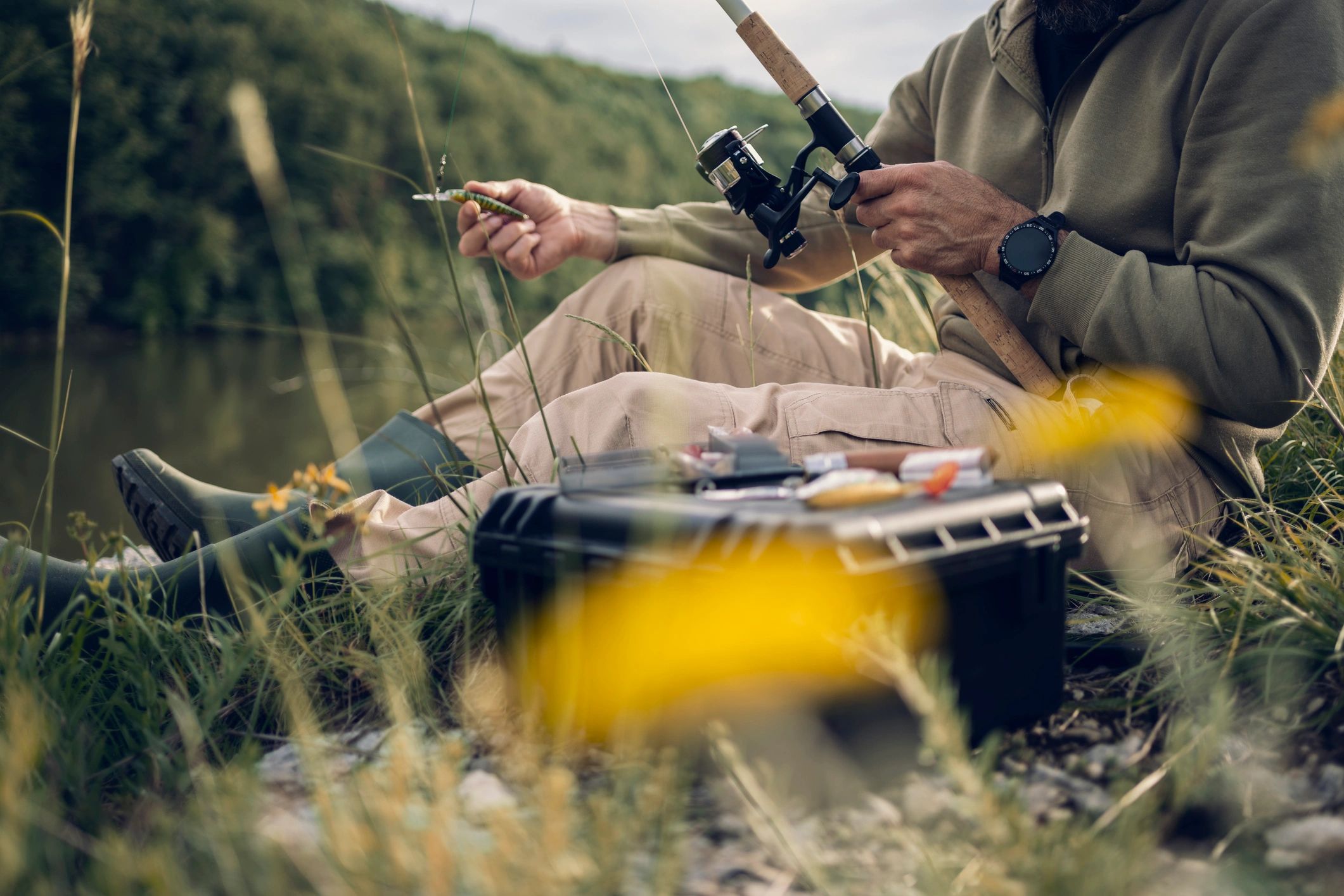 Hands preparing fishing bait outdoors near the water