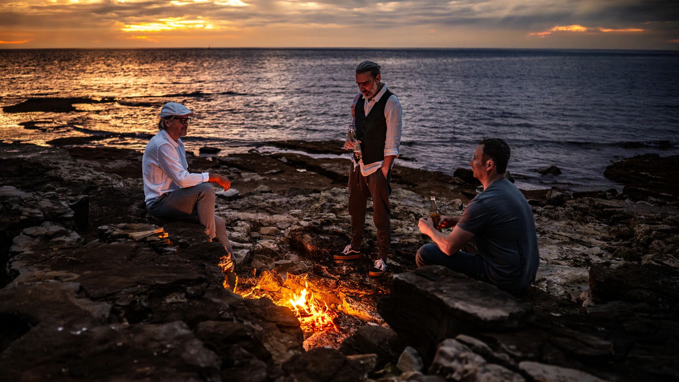 Campfire gathering outdoors near water at sunset